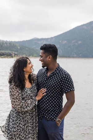 A couple shares a romantic moment by a scenic mountain lake wearing coordinated polka dot and floral patterns.