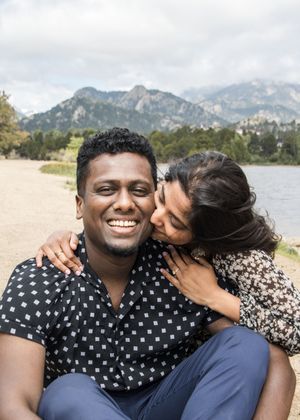 A loving couple shares a tender moment by a mountain lake with scenic peaks in the background.