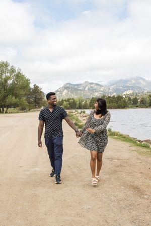 A couple takes a romantic walk along a lakeside path with mountain views in the background.
