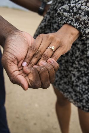 Two hands intertwined showing a close-up of engagement or wedding rings in an intimate moment.