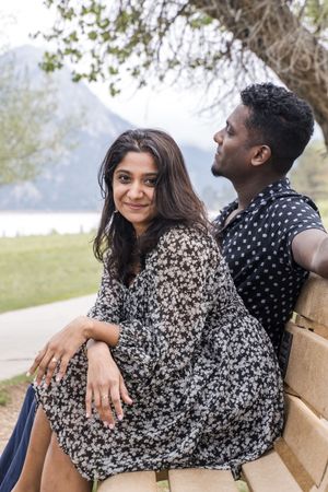 Couple sharing a romantic moment on a bench by a scenic lake with mountains in the background.