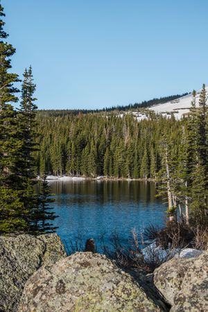 Snow-capped mountain reflects in a pristine alpine lake surrounded by evergreen forest on a clear day.