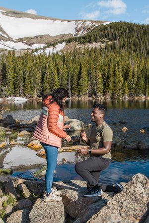 A surprise proposal moment captured on rocky terrain by a mountain lake.