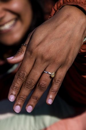 Close-up of a sparkling engagement ring on a hand against a coral-colored background.