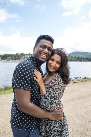 A happy couple embraces by a scenic lakeside while wearing coordinating polka dot and floral print outfits.