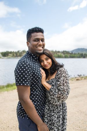 A loving couple in matching black and white patterned outfits embraces near a lake.