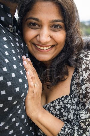 Close-up shot showing an engagement ring while wearing a floral dress and leaning against a polka dot shirt.