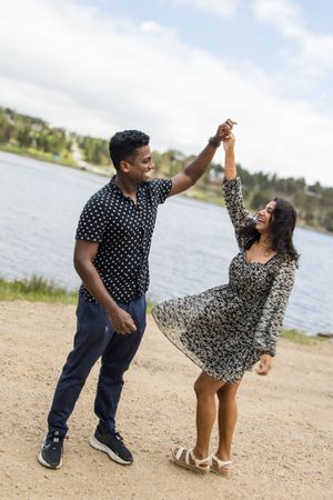 A couple dances joyfully on a lakeside path, their coordinated outfits swaying with the movement.