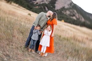 Couple embraces in golden field with mountains in background during sunset photo session.