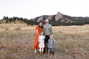 Family poses together in a rustic field with mountains and evergreen trees in the background during golden hour.