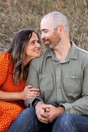 A couple shares an intimate moment outdoors, with her wearing a red polka dot dress and him in a gray button-down shirt.