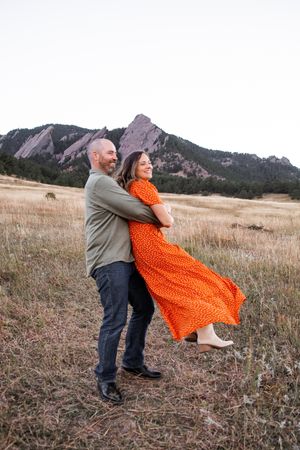 A couple dances playfully in a field with the majestic Flatirons rock formations visible in the background near Boulder.