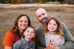 A family laughs together while sitting outdoors during an autumn photo session.