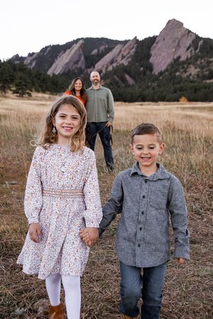 Two people walk together in a field with the iconic Flatiron rock formations of Boulder, Colorado in the background.
