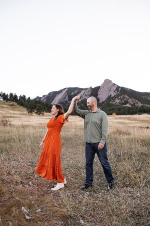 A couple dances playfully in a field with the Flatirons rock formation visible in the background near Boulder, Colorado.