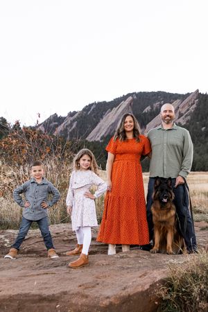 A family poses together with their German Shepherd dog against the backdrop of the Flatirons rock formations in Boulder, Colorado.