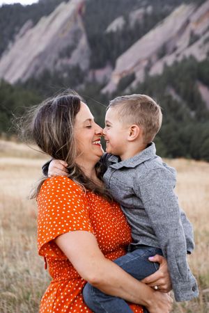 A tender moment shared between parent and child against a backdrop of mountain cliffs and grassy fields.