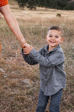 A young child in a gray button-up shirt and jeans plays joyfully in a grassy autumn field.