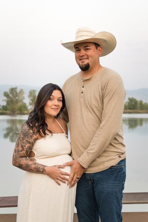 Romantic couple in rustic attire embrace near a serene lake during a sunset photoshoot.