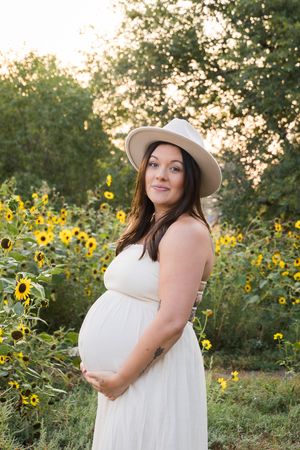 Figure in white dress and sun hat poses among vibrant sunflower field during golden hour.