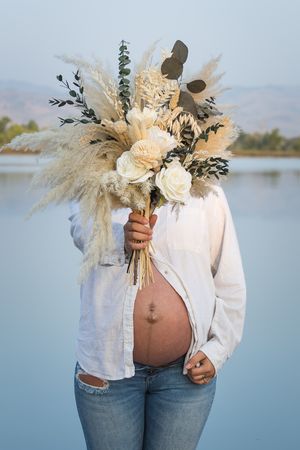 Bohemian maternity photoshoot progression showing growing belly with white roses and pampas grass bouquet against blue lake.