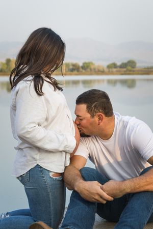 Romantic couple sits by a serene lake during an outdoor engagement photoshoot session at sunset.
