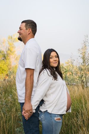A couple embraces in a sunny field of tall grass and wildflowers on a warm afternoon.