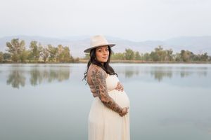Two people share a tender moment by a serene lake during a maternity photo session in nature.