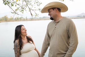Expectant couple wearing casual attire share a joyful moment together near a peaceful lake.