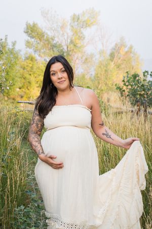 A person wearing a cream-colored dress poses in a field of tall grass during golden hour with natural sunlight.