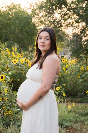 A flowing white dress stands out against a backdrop of vibrant yellow sunflowers in a natural outdoor setting during golden hour.