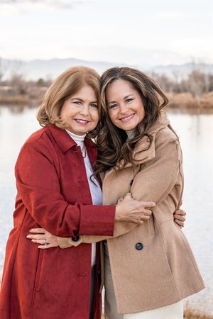 Two people in winter coats share a warm embrace outdoors by a lake on a cold day.