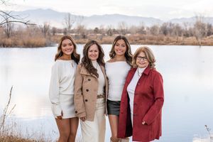 A group of friends pose together outdoors near a lake on a winter day wearing stylish coats and sweaters.