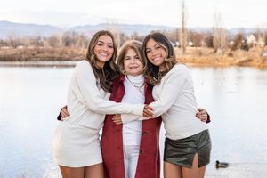 A group in coordinated winter outfits of white sweaters and burgundy scarves poses together outdoors near a lake.