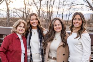 A group of friends pose together outdoors wearing casual winter attire and smiling on a wooden walkway.