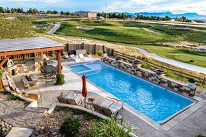 Aerial view of a luxury outdoor pool with patio seating, pergola, and scenic green landscape in the background.