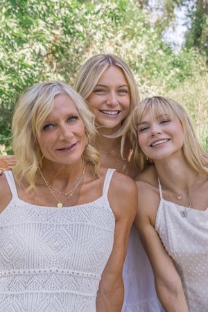 Two people in matching white outfits share joyful laughter while sitting close together outdoors.
