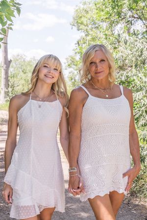 Two people walking outdoors wearing white crochet summer dresses and holding hands on a sunny day.