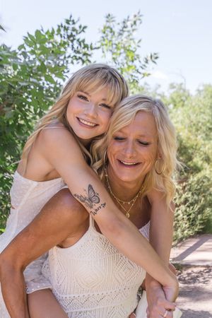 Two people embrace and laugh together while wearing white summer dresses in a natural outdoor setting.