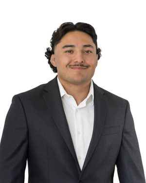 Professional headshot of person in dark suit and white shirt against white background.