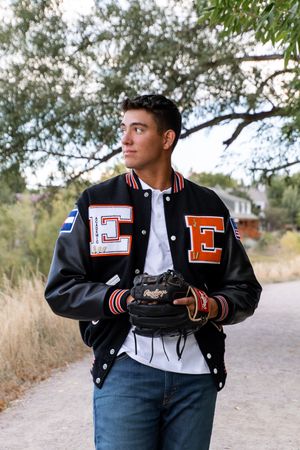 Person in black varsity jacket poses casually on path with scenic backdrop.