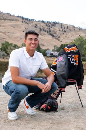 A letterman jacket and backpack displayed on a chair against a scenic hillside backdrop.