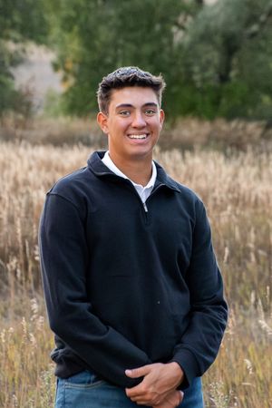 A person wearing a black pullover sits in an outdoor field with tall grass and natural lighting in the background.