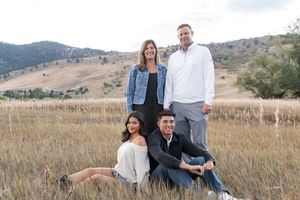 A group poses together in casual attire against a scenic mountain landscape with tall grass during golden hour.