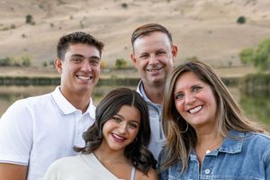 A group gathers outdoors near a lake for a casual family photo shoot on a sunny day.