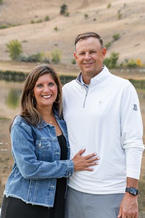 A couple in casual clothing poses for portraits outdoors in a desert landscape with hills in the background.