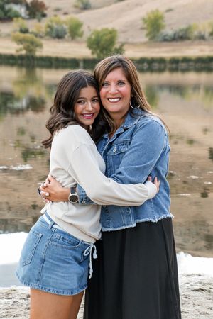 Two people hugging and smiling while posing together by a lake during sunset.