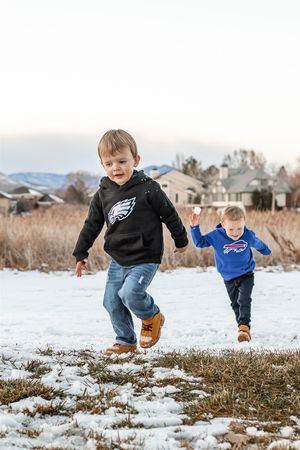 People jumping and playing in a snowy field with houses and mountains in the distance.
