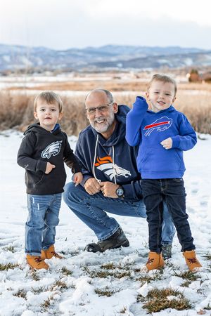 Three generations pose together in winter snow wearing NFL team apparel including Eagles and Bills hoodies.