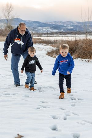 Two people playfully run through fresh snow on a winter day with mountains visible in the background.